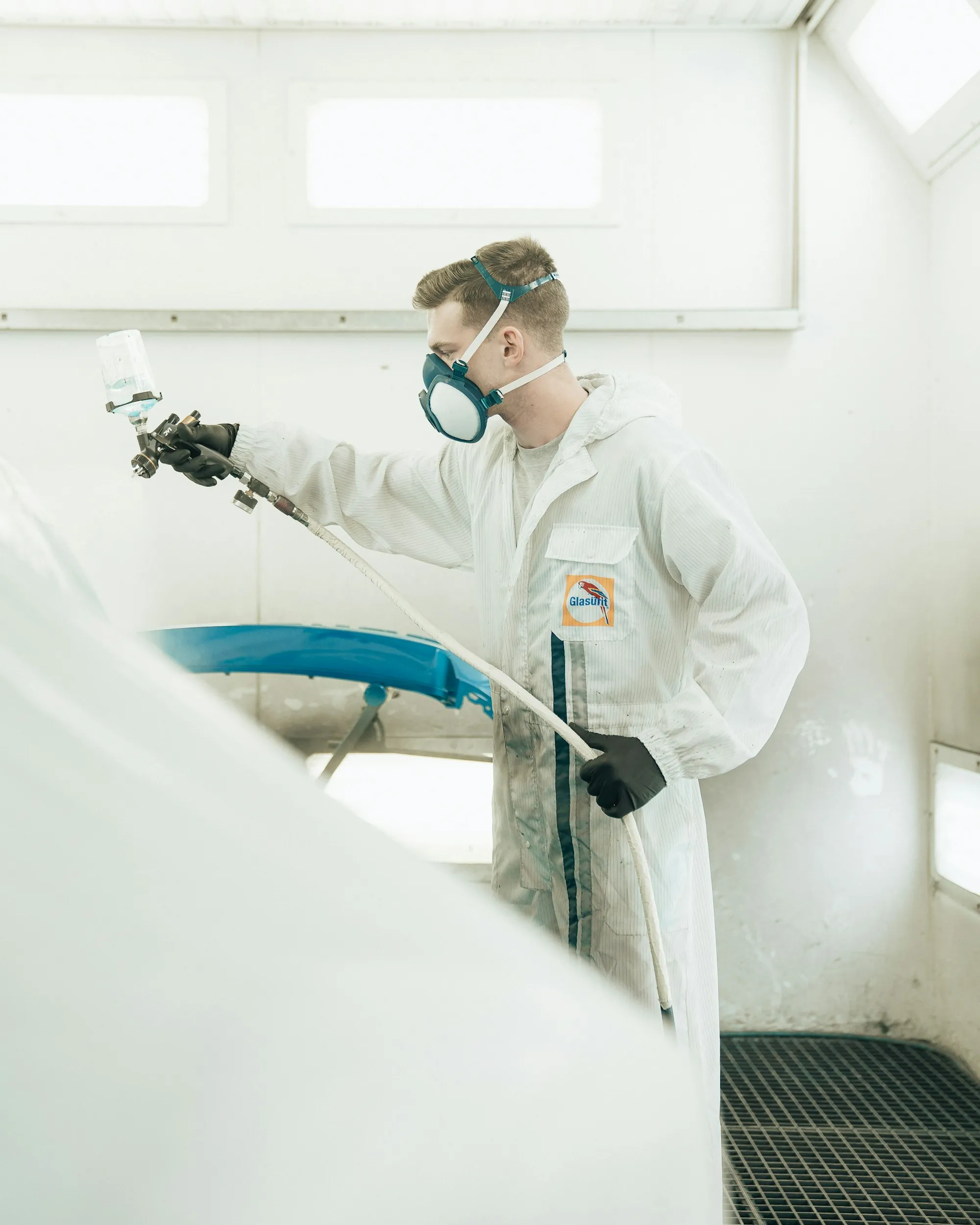 Painter in a protective suit spraying a car