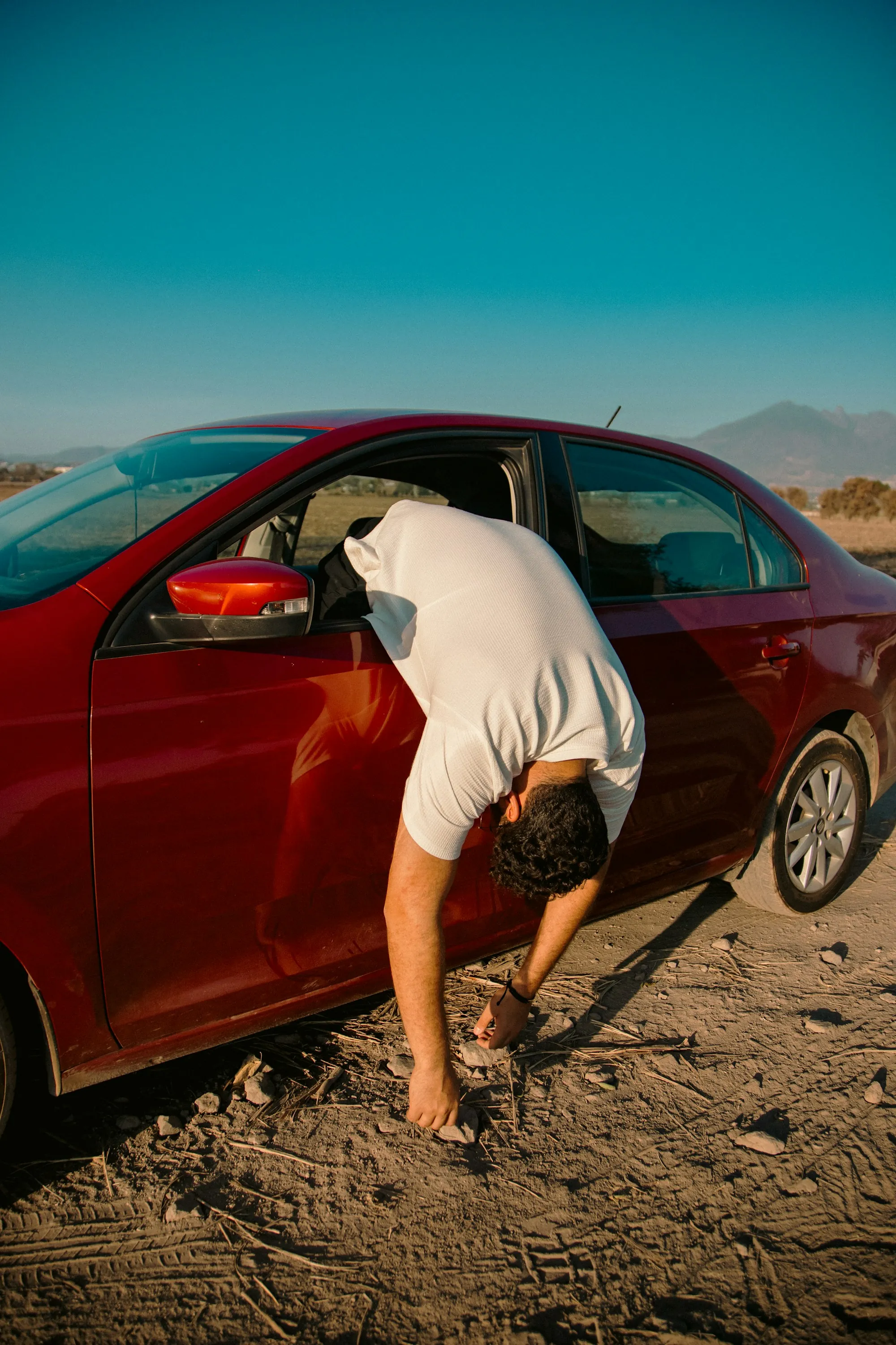Technician fitting a repaired front fender onto a blue hatchback in a body shop