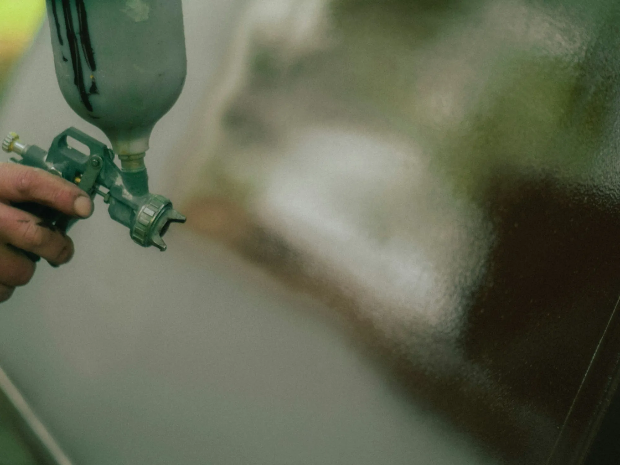 Painter in a protective suit spraying a car door inside a downdraft paint booth