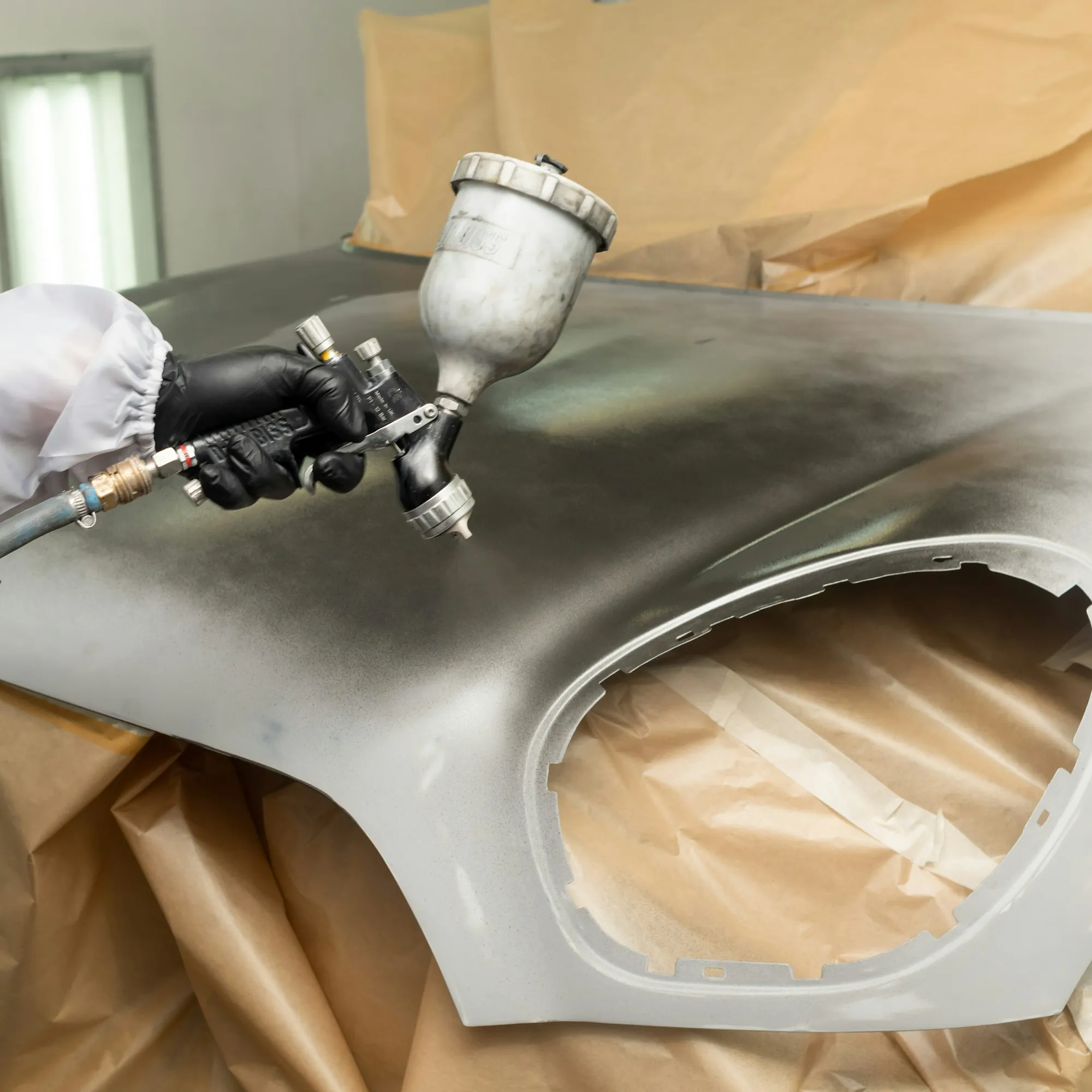 Painter in a protective suit spraying a car panel
